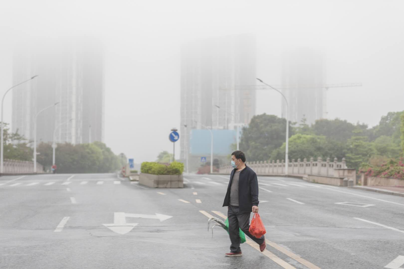佛山顺德陈村,缤纷一路上,一市民提着肉菜过马路,不远处的高楼笼罩在雨雾中。图/佛山日报记者王伟楠摄